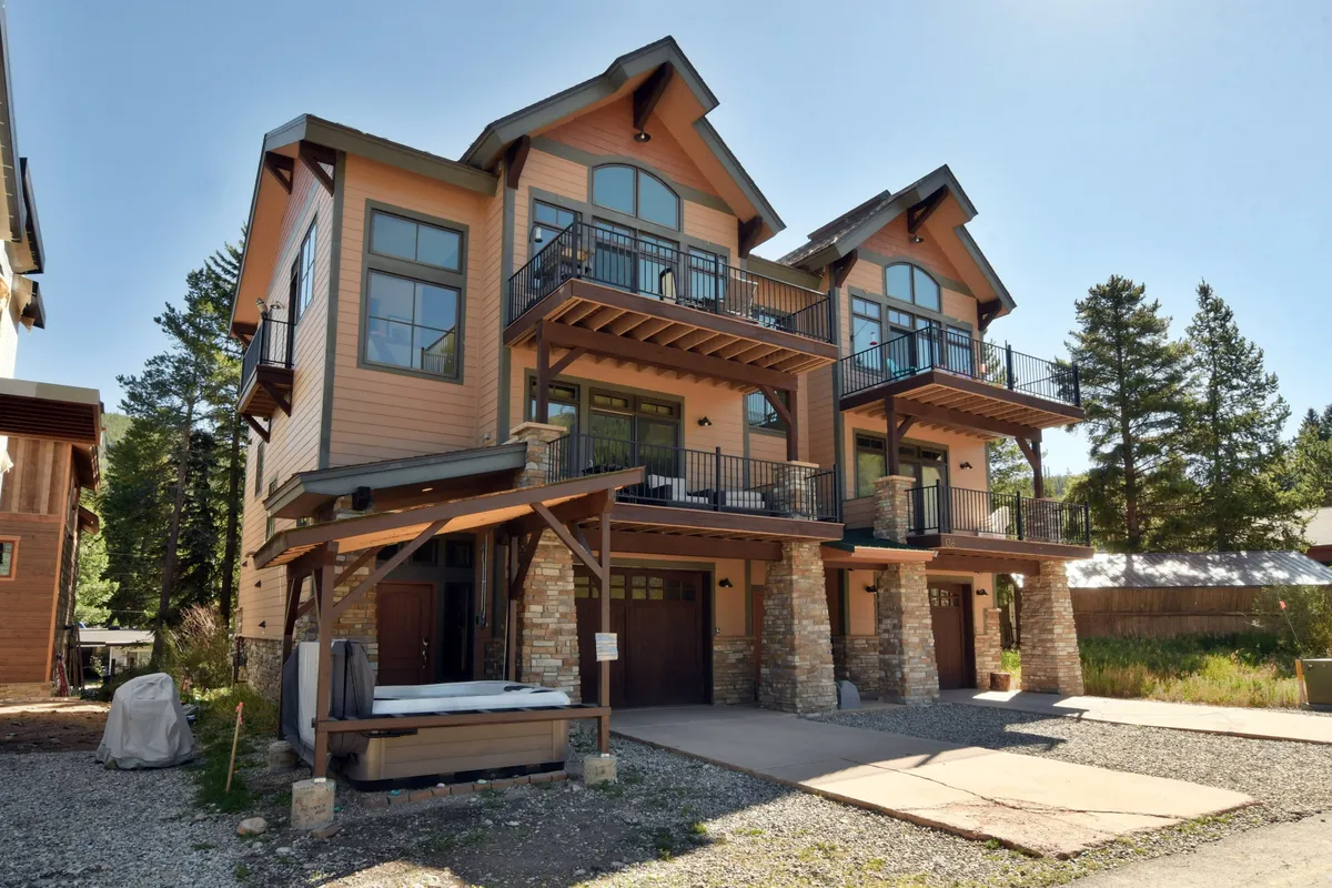 The image showcases a beautiful multi-story villa with stone accents, spacious balconies, and large inviting garage doors. The home exudes mountain charm and luxury, set against the scenic backdrop of Winter Park. The balconies are perfect for relaxing, watching sunsets, or gathering with friends and family after a day of adventures.