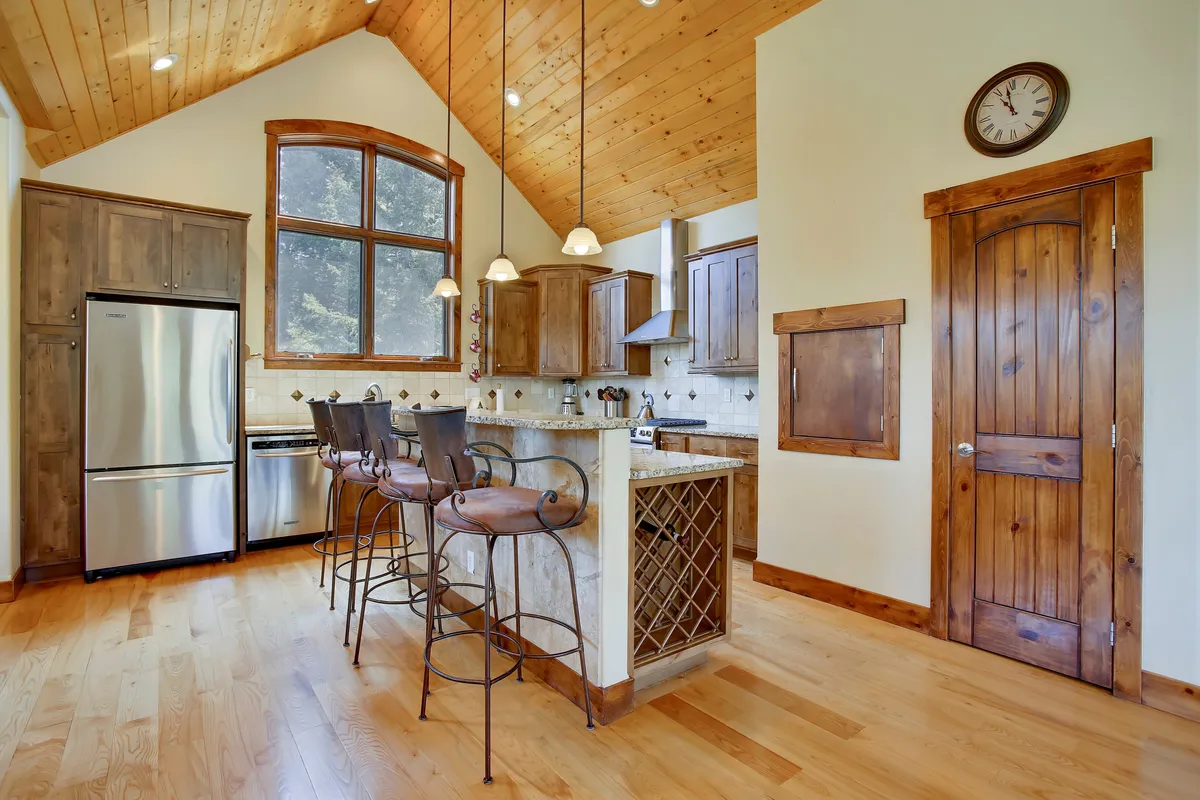 This image highlights a kitchen island with bar stools, wooden cabinetry, and large windows that fill the space with natural light. The setting is ideal for casual dining, cooking lessons, or family brunches, blending comfort with functionality.