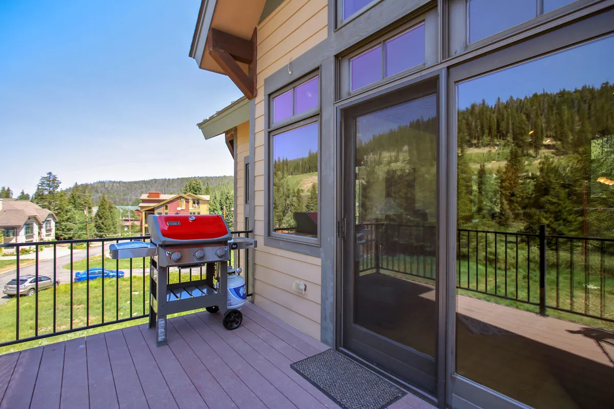 An exterior deck featuring a grill and balcony railing, set against a stunning backdrop of mountain vistas. The space is designed for barbecuing, relaxing, and gathering with friends, extending the living area outdoors for al fresco dining and breathtaking views.