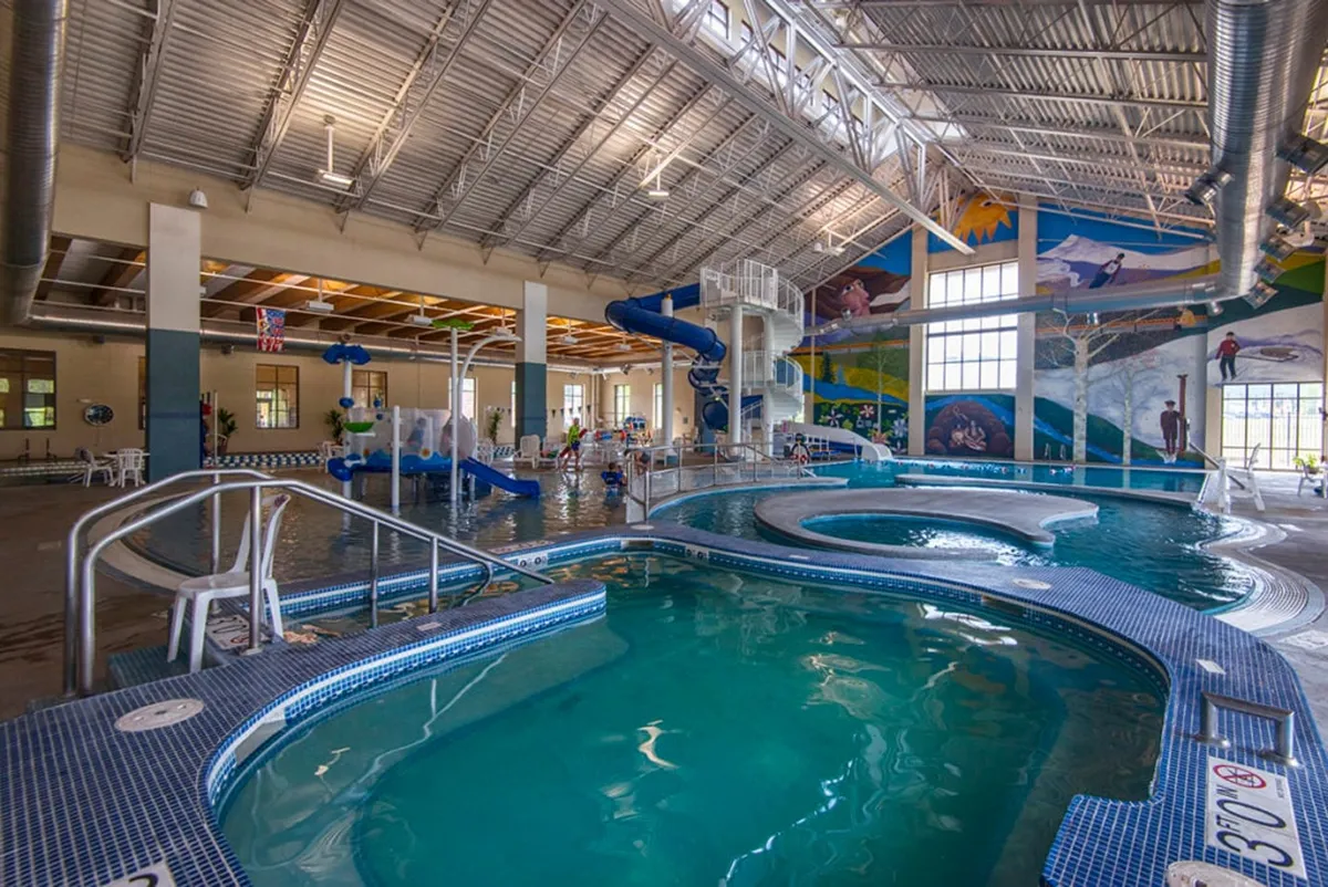 This image captures the lively atmosphere of the Grand Park Rec Center, with children playing on water slides, splashing in the bright swimming pools, and colorful murals adding a cheerful vibe. The visible joy and group activities illustrate the family-friendly amenities available nearby.