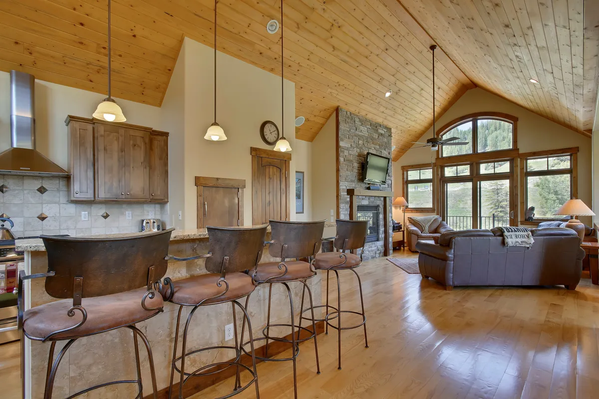 A cozy yet elegant seating area with a stone fireplace, bar counter with stools, and large windows offering scenic mountain views. The space feels inviting for both relaxation and entertaining.