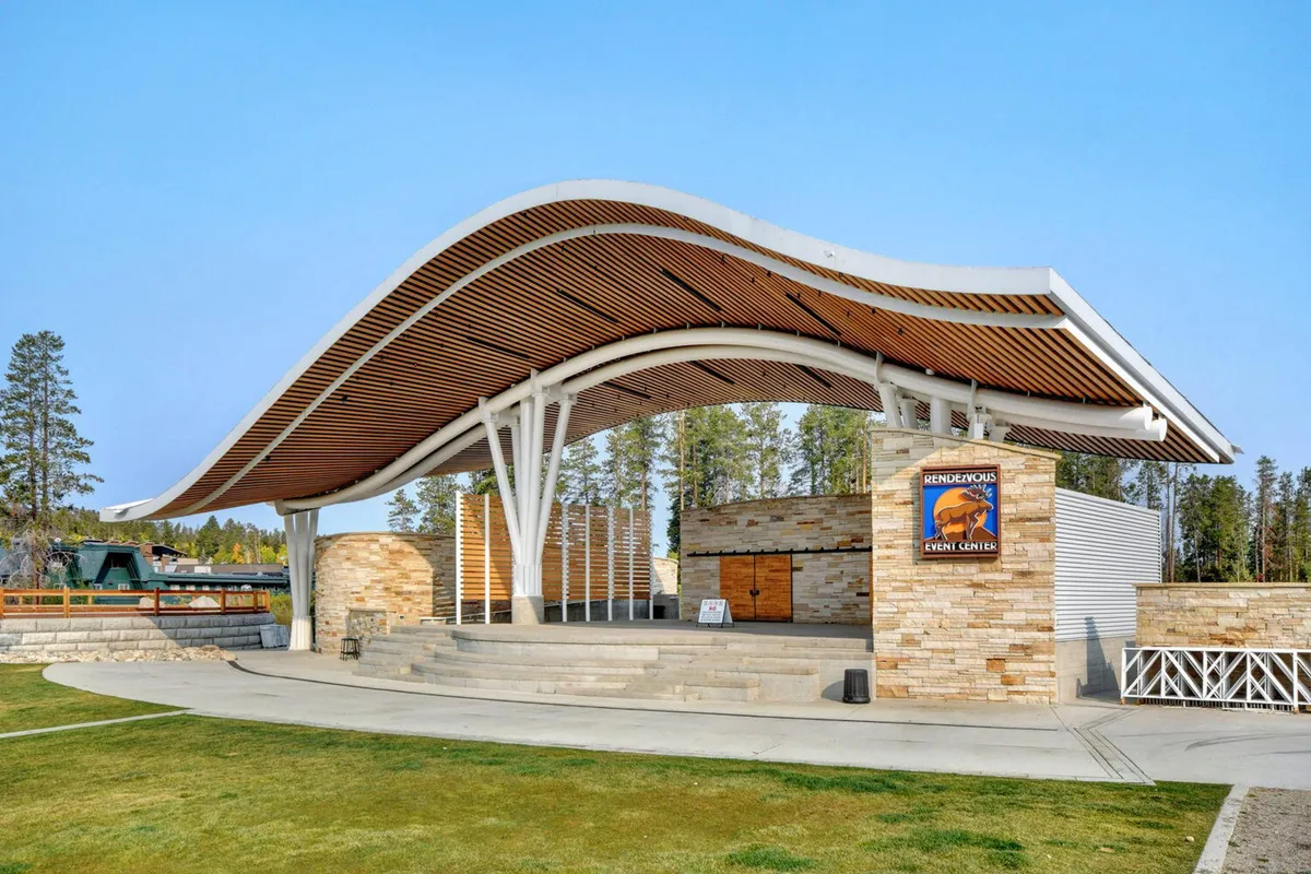 An exterior shot featuring the unique, wave-like roof structure and stone façade of a community venue, with a welcoming wooden deck. The scene hints at outdoor events, community gatherings, and festive seasonal celebrations that bring families together in the neighborhood.