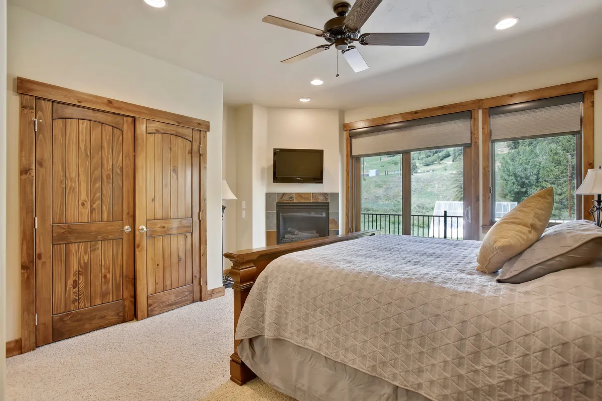 A king-sized bed is the centerpiece of this spacious bedroom, surrounded by large windows that fill the room with natural light. Wooden furniture, soft textiles, and a fireplace add to the atmosphere of relaxation and comfort, creating an inviting sanctuary for restful nights and peaceful mornings.