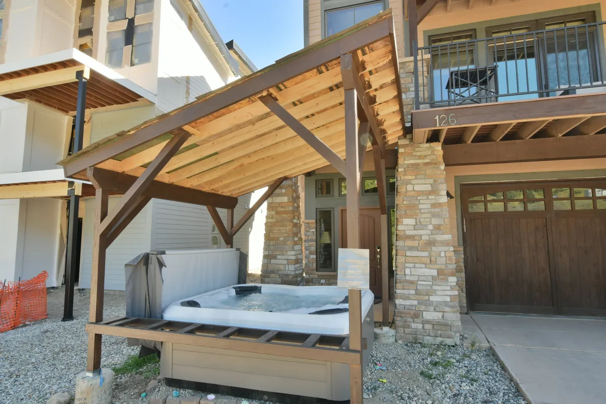 A steaming hot tub set on a wooden deck supported by stone pillars, offering picturesque views for sunset or morning relaxation. The setting is enveloped in nature, highlighting both comfort and exclusivity.