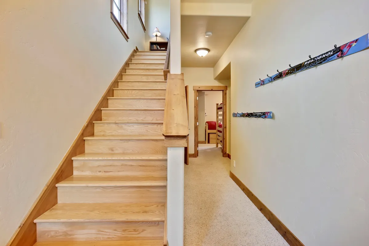 A bright, inviting entryway with a staircase, wall hooks, and a doorway, evoking the feeling of arriving to a warm family home. The scene suggests everyday comings and goings, and the little moments families share as they head out for adventures or return from outings.