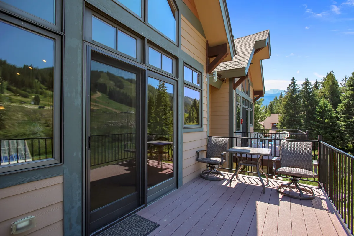 An inviting outdoor patio with comfortable furniture overlooking a stunning mountain view, accessed through glass doors. The scene is tranquil, suggesting a perfect spot for relaxing, dining, or soaking in the scenery after a day of adventure.
